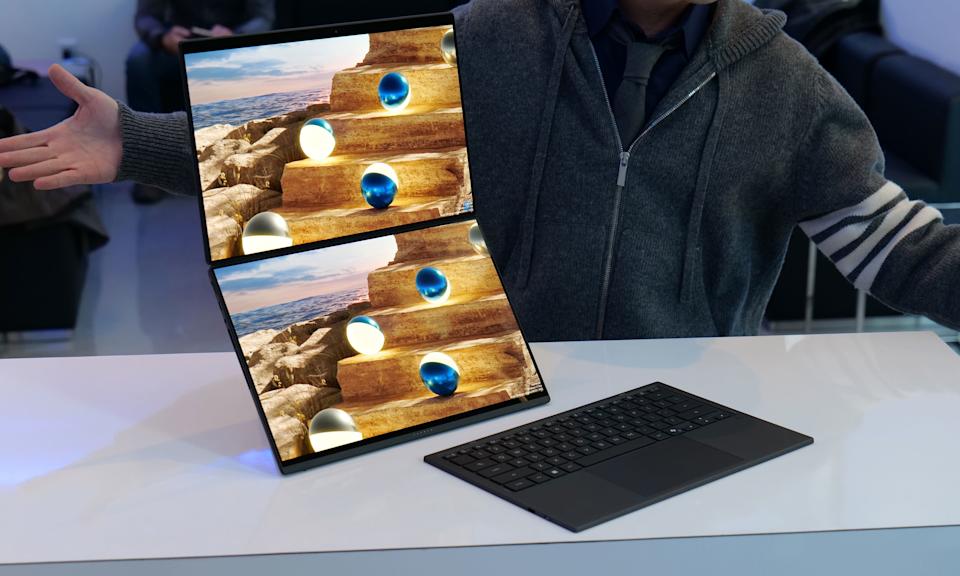 لپ‌تاپ Zenbook Duo با دو صفحه نمایش لمسی که به صورت عمودی روی هم باز شده‌اند و کیبورد در کنار آن‌ها قرار دارد.