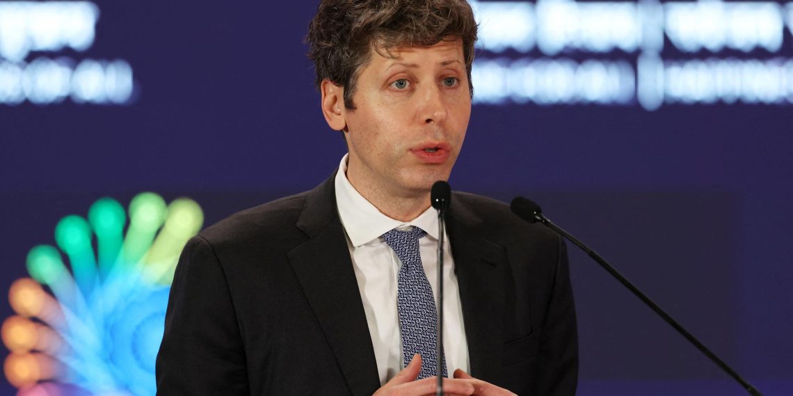 تصویر خبری از ارائه رسمی در یک رویداد فناوری یا اقتصادی که سم آلتمن با کتوشلوار پشت تریبون قرار دارد و از میکروفن استفاده میکند. پسزمینه شامل گرافیکهای رنگی و عناصر بصری مرتبط با نوآوری، داده و فناوریهای پیشرفته است و فضای کلی تصویر به سیاستگذاری یا استراتژیهای مرتبط با هوش مصنوعی اشاره دارد.