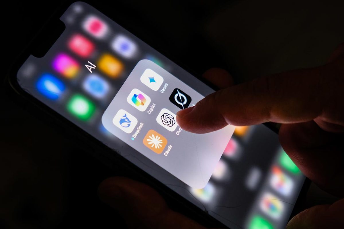 نمای نزدیک از صفحهنمایش گوشی هوشمند که پوشهای با عنوان AI را نشان میدهد؛ آیکنهای ChatGPT، Google Gemini، Microsoft Copilot و Claude در کنار یکدیگر دیده میشوند و انگشتی در حال لمس آیکن ChatGPT است