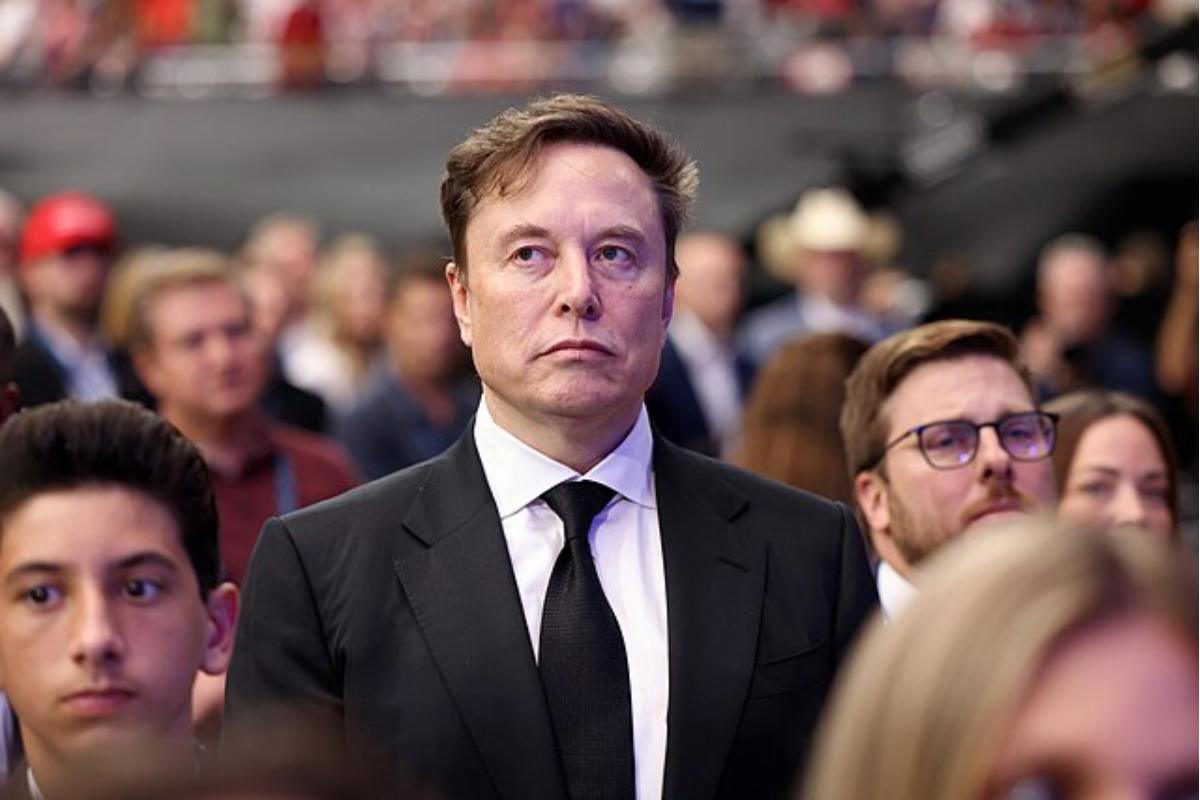 نمایی از یک رویداد رسمی یا مراسم عمومی که در آن فردی با پوشش رسمی در مرکز تصویر قرار دارد و اطراف او جمعی از حاضران دیده میشوند. عمق میدان کم باعث محو شدن پسزمینه شده و تمرکز تصویر بر فضای رویداد، حضور جمعی و حالوهوای مراسم رسمی است.