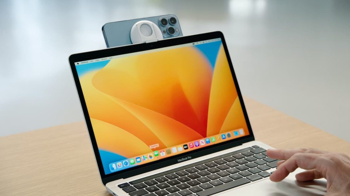 یک گوشی آیفون که با استفاده از پایه مخصوص به بالای صفحه نمایش مک‌بوک متصل شده است.