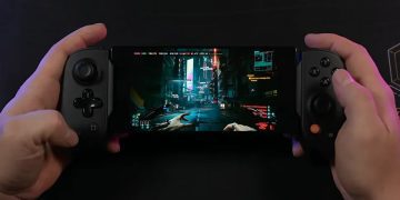 نمای یک گوشی هوشمند که به کنترلر گیمینگ فیزیکی دوطرفه متصل شده و بازی Cyberpunk 2077 را در حالت نمای اول‌شخص اجرا می‌کند. تصویر خیابان‌های نئونی شهر Night City با نورپردازی سایبرپانکی روی نمایشگر دیده می‌شود و این صحنه اجرای بازی AAA روی موبایل را نمایش می‌دهد.