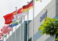 نمای بیرونی ساختمان شرکت SMIC با ردیفی از پرچم کشورهای مختلف در حال اهتزاز.