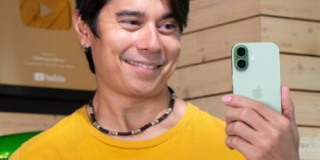 مردی در حال لبخند زدن و نگاه کردن به پشت یک گوشی آیفون ۱۶ سبز رنگ.