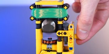 نمای نزدیک موتور لگویی در حال چرخش با سیم‌پیچ سبزرنگ، روتور آهنربایی و دست کاربر در حال چرخاندن محور جانبی