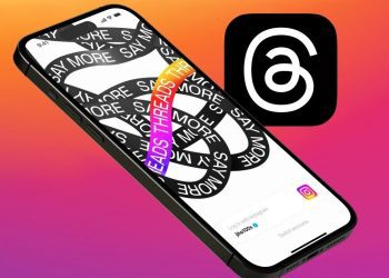نمای مایل از یک آیفون که طرح گرافیکی "Say More" روی آن است و لوگوی برنامه Threads در کنار آن دیده می‌شود.