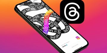 نمای مایل از یک آیفون که طرح گرافیکی "Say More" روی آن است و لوگوی برنامه Threads در کنار آن دیده میشود.