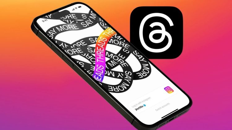 نمای مایل از یک آیفون که طرح گرافیکی "Say More" روی آن است و لوگوی برنامه Threads در کنار آن دیده می‌شود.