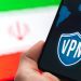 دستی که گوشی هوشمندی با نماد VPN و نقشه جهان را در مقابل پرچم ایران نگه داشته است.