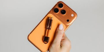 یک گوشی آیفون نارنجی که کابل شارژ کوچک ChargeKey برند نوماد با همان رنگ روی آن قرار گرفته است.