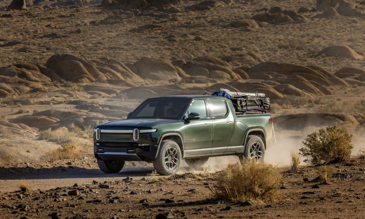 وانت پیکاپ ریویان سبز رنگ در حال رانندگی در یک جاده خاکی بیابانی با تجهیزات کمپینگ.