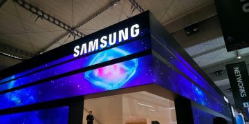 تابلوی بزرگ تبلیغاتی سامسونگ با نورپردازی آبی و بنفش و پسزمینه فضایی در نمایشگاه فناوری داخل سالن، همراه با لوگوی روشن SAMSUNG در بالای غرفه