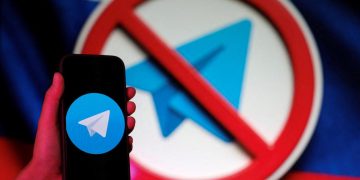 تصویر مفهومی از اپلیکیشن پیام‌رسان Telegram که روی صفحه یک گوشی هوشمند نمایش داده شده و در پس‌زمینه، نماد ممنوعیت (Prohibition Sign) روی لوگوی تلگرام دیده می‌شود. این تصویر به محدودسازی، فیلترینگ یا مسدودسازی تلگرام در یک کشور و چالش‌های دسترسی به پیام‌رسان‌ها اشاره دارد.