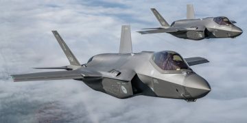 دو جنگنده اف-۳۵ خاکستری‌رنگ در حال پرواز در ارتفاع بالا بر فراز ابرها در آرایش دوتایی کنار یکدیگر دیده می‌شوند.