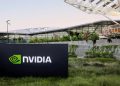 تابلوی NVIDIA در محوطه بیرونی ساختمان مدرن شرکت با معماری شیشهای و فضای سبز، نماد دفتر مرکزی و زیرساخت شرکتی انویدیا
