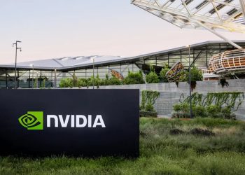 تابلوی NVIDIA در محوطه بیرونی ساختمان مدرن شرکت با معماری شیشه‌ای و فضای سبز، نماد دفتر مرکزی و زیرساخت شرکتی انویدیا