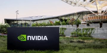 تابلوی NVIDIA در محوطه بیرونی ساختمان مدرن شرکت با معماری شیشه‌ای و فضای سبز، نماد دفتر مرکزی و زیرساخت شرکتی انویدیا