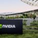 تابلوی NVIDIA در محوطه بیرونی ساختمان مدرن شرکت با معماری شیشهای و فضای سبز، نماد دفتر مرکزی و زیرساخت شرکتی انویدیا
