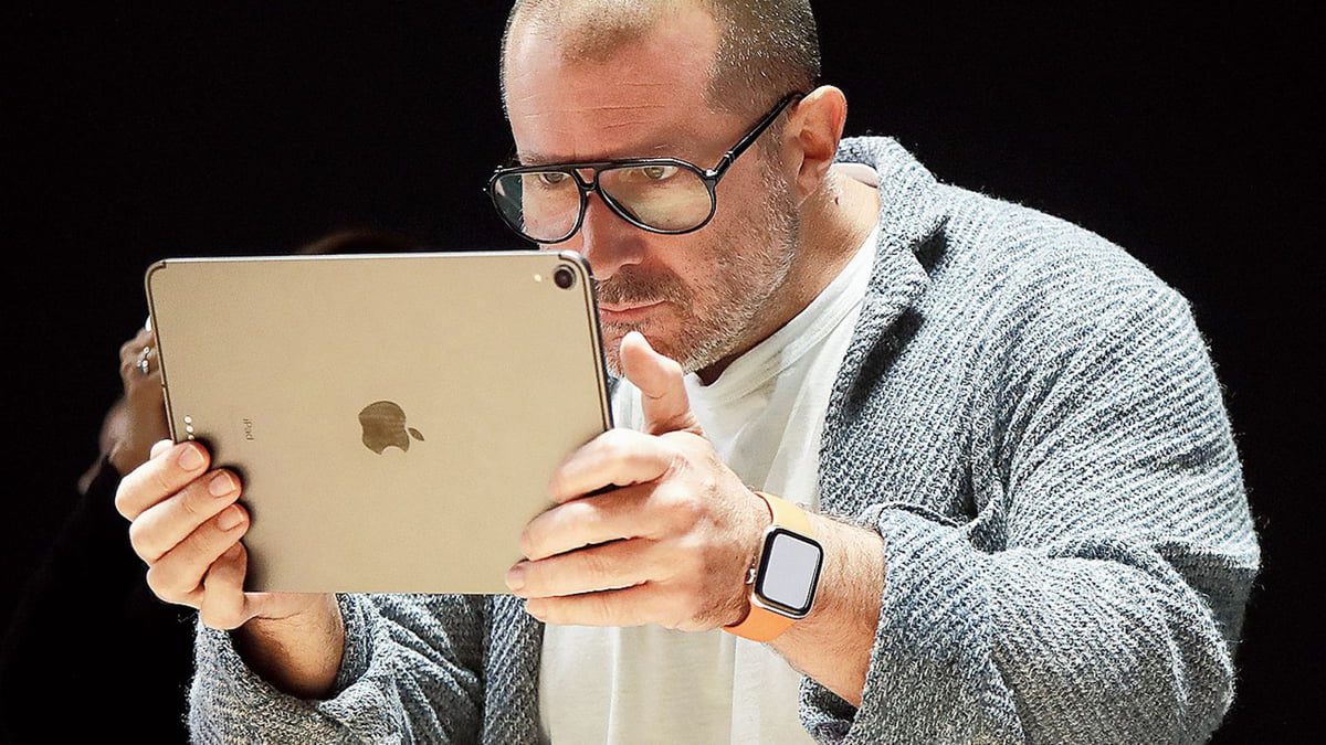 تصویری از یک تبلت Apple iPad Pro با بدنه فلزی نقره‌ای که به‌صورت افقی در دست جانی آیو گرفته شده است؛ لوگوی اپل در مرکز پنل پشتی دیده می‌شود و طراحی مینیمال دستگاه با لبه‌های صاف و ضخامت کم در نور استودیویی برجسته شده است.