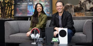 فیل اسپنسر و آشا شارما نشسته روی مبل در فضای معرفی محصولات گیمینگ، با نمایش کنسول Xbox، کنترلرها و هدست، در پسزمینهای مرتبط با بازیهای ویدیویی و اکوسیستم Xbox