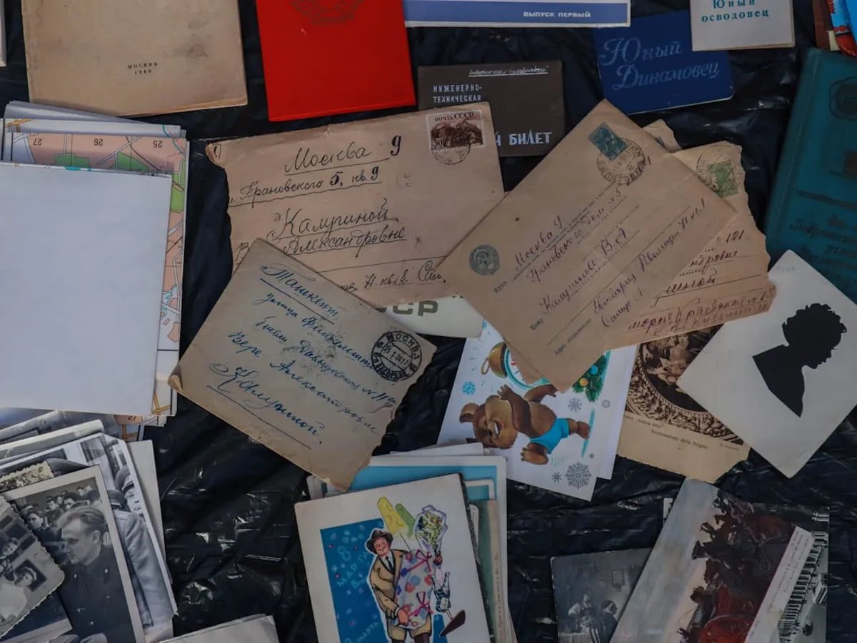 مجموعهای از نامهها، کارتپستالها و عکسهای قدیمی نوشتهشده به زبان روسی روی میز؛ شامل پاکتهای پستی، دفترچهها و تصاویر چاپی دوران تاریخی شوروی