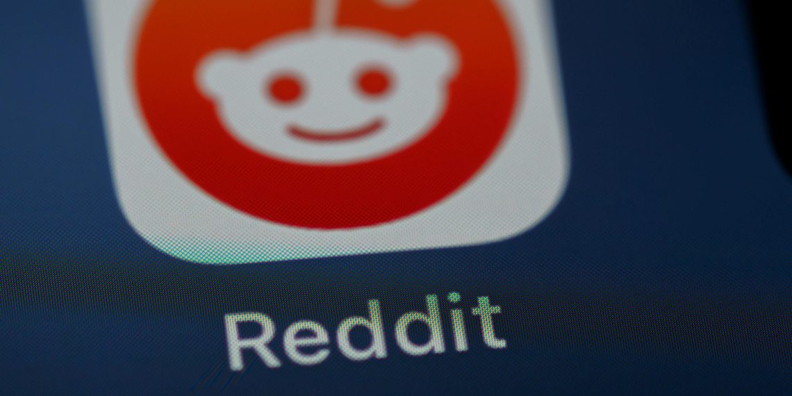 نمای نزدیک از آیکون اپلیکیشن Reddit روی صفحه نمایش گوشی هوشمند با پسزمینه تیره