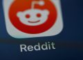 نمای نزدیک از آیکون اپلیکیشن Reddit روی صفحه نمایش گوشی هوشمند با پسزمینه تیره