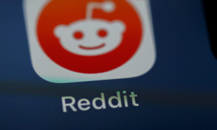 نمای نزدیک از آیکون اپلیکیشن Reddit روی صفحه نمایش گوشی هوشمند با پسزمینه تیره