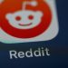 نمای نزدیک از آیکون اپلیکیشن Reddit روی صفحه نمایش گوشی هوشمند با پس‌زمینه تیره