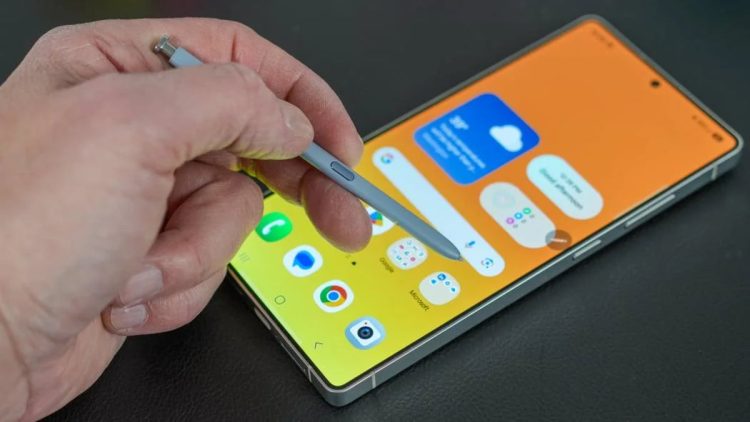 نمای نزدیک از دست کاربر که با قلم S Pen بر روی صفحه‌نمایش یک گوشی هوشمند سامسونگ با پس‌زمینه زرد/نارنجی در حال کار است؛ تأکید بر قابلیت‌های یادداشت‌برداری و دقت قلم روی رابط کاربری One UI