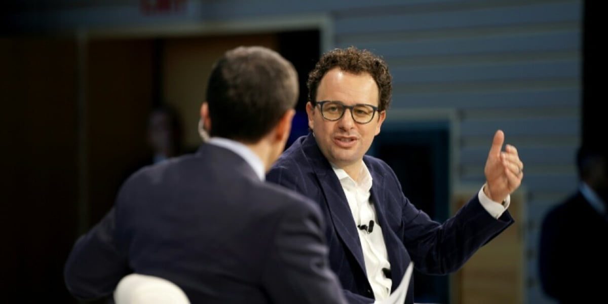 صحنه گفتوگو در رویداد رسمی؛ دو نفر نشسته روی صندلیهای سفید در حال بحث روی صحنه با پسزمینه آبی و نور متمرکز— نمایی از جلسه یا کنفرانس مرتبط با فناوری و هوش مصنوعی