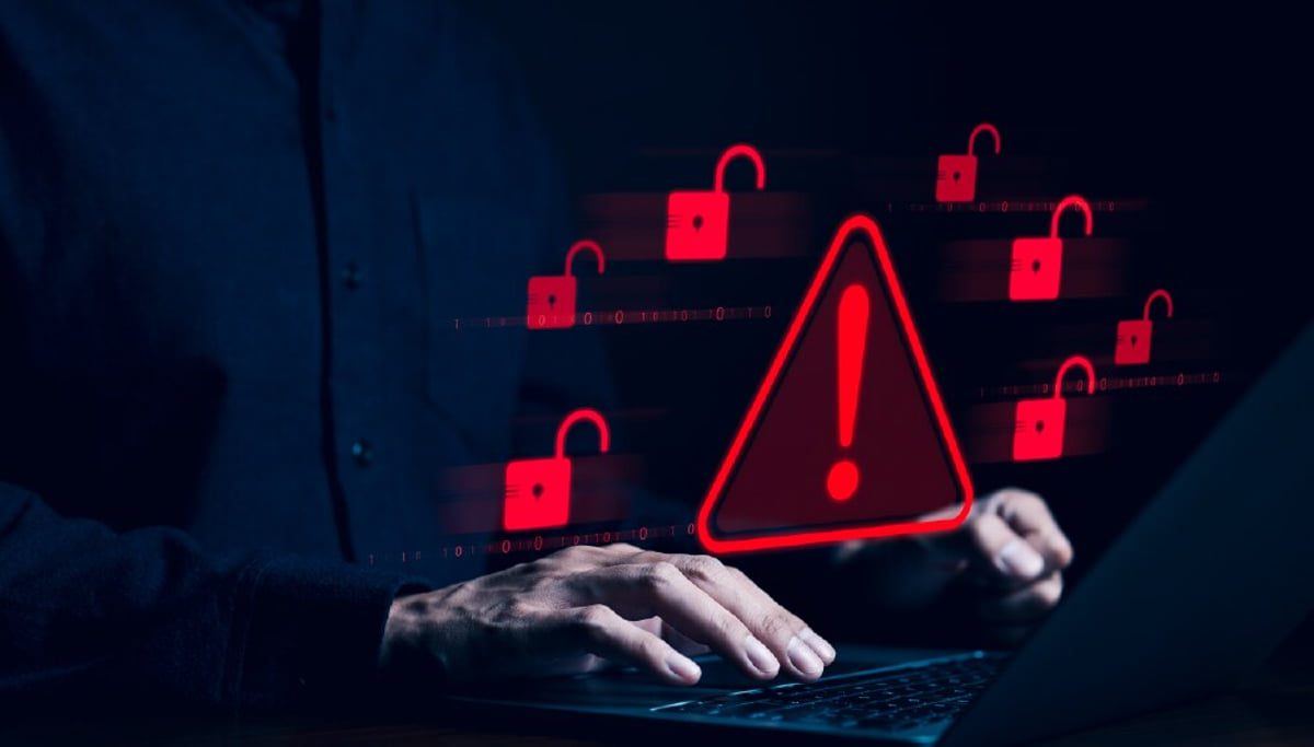 دست‌های کاربر در حال تایپ روی لپ‌تاپ در تاریکی، همراه با نمادهای هشداری قرمز رنگ قفل باز شده و یک مثلث هشدار بزرگ؛ نمایش نفوذ، اکسپلویت (Exploit) و تهدیدات ویروسی سال ۲۰۲۴