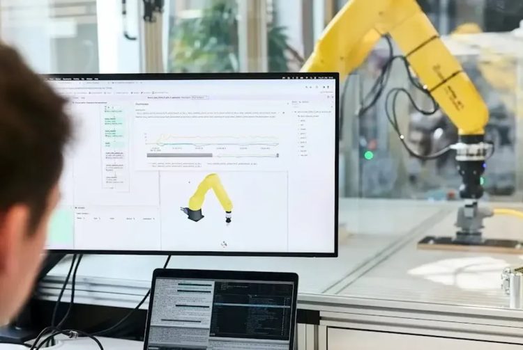 یک بازوی ربات زرد در حال تست در آزمایشگاه و نمایش حرکات آن روی مانیتور کامپیوتر
