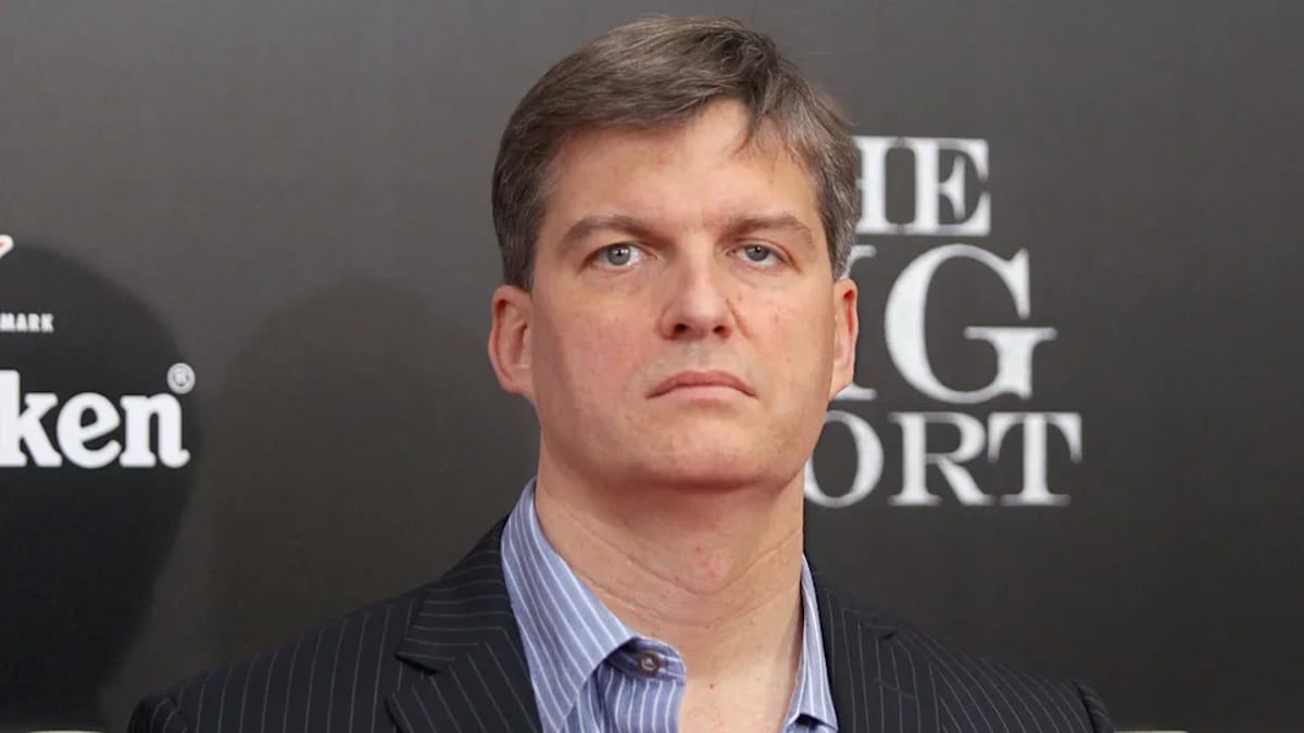 پرتره کلوزآپ از مایکل بری (Michael Burry)، سرمایهگذار مشهور و مدیر صندوق تامین سرمایه، با کت و شلوار راه راه و پیراهن آبی، در حال شرکت در یک رویداد تبلیغاتی فیلم The Big Short با پسزمینه برند Heineken