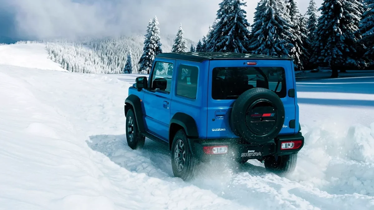 نمای عقب خودروی آفرود Suzuki Jimny 2026 در حال حرکت روی مسیر برفی کوهستان با لاستیک زاپاس در درِ صندوق