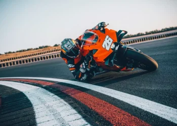 موتورسیکلت KTM 990 RC R نارنجی در حال پیچیدن سریع در پیست مسابقه با راننده‌ی مجهز به لباس ریسینگ کامل.