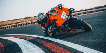 موتورسیکلت KTM 990 RC R نارنجی در حال پیچیدن سریع در پیست مسابقه با رانندهی مجهز به لباس ریسینگ کامل.