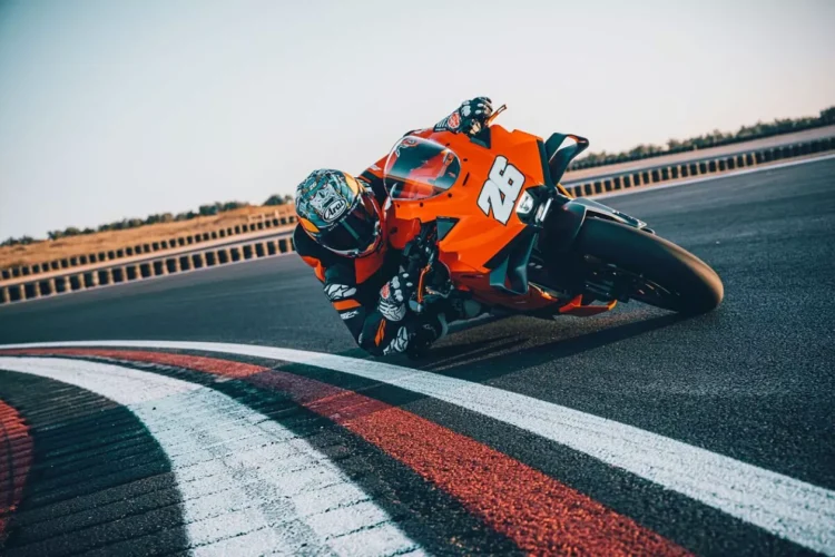 موتورسیکلت KTM 990 RC R نارنجی در حال پیچیدن سریع در پیست مسابقه با رانندهی مجهز به لباس ریسینگ کامل.