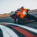 موتورسیکلت KTM 990 RC R نارنجی در حال پیچیدن سریع در پیست مسابقه با راننده‌ی مجهز به لباس ریسینگ کامل.