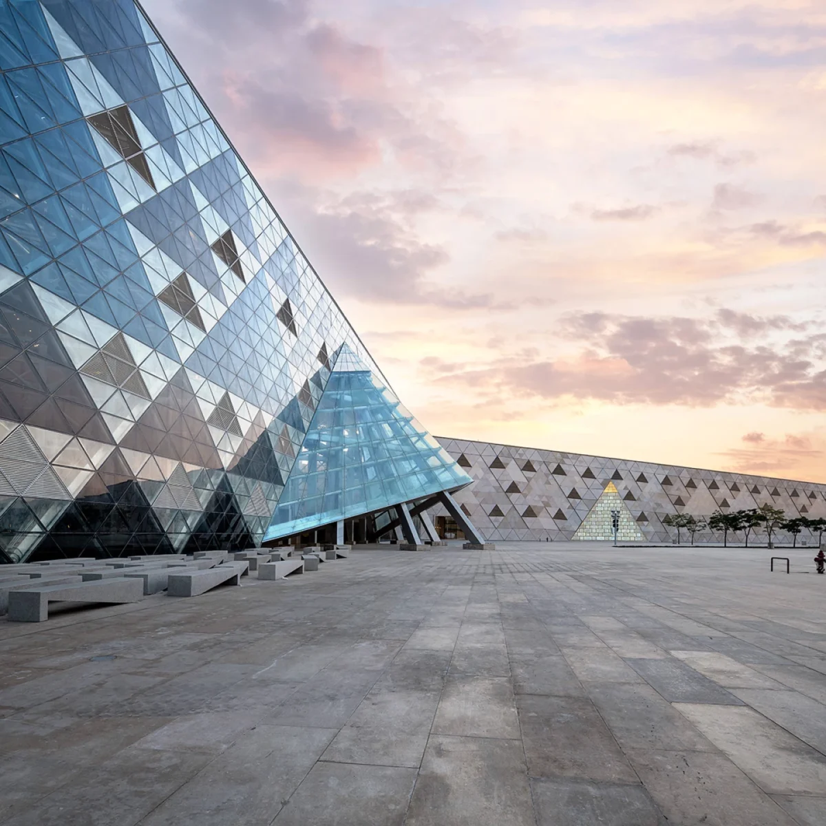 نمای شیشهای مدرن موزه بزرگ مصر با انعکاس آسمان غروب بر شیشههای مثلثی