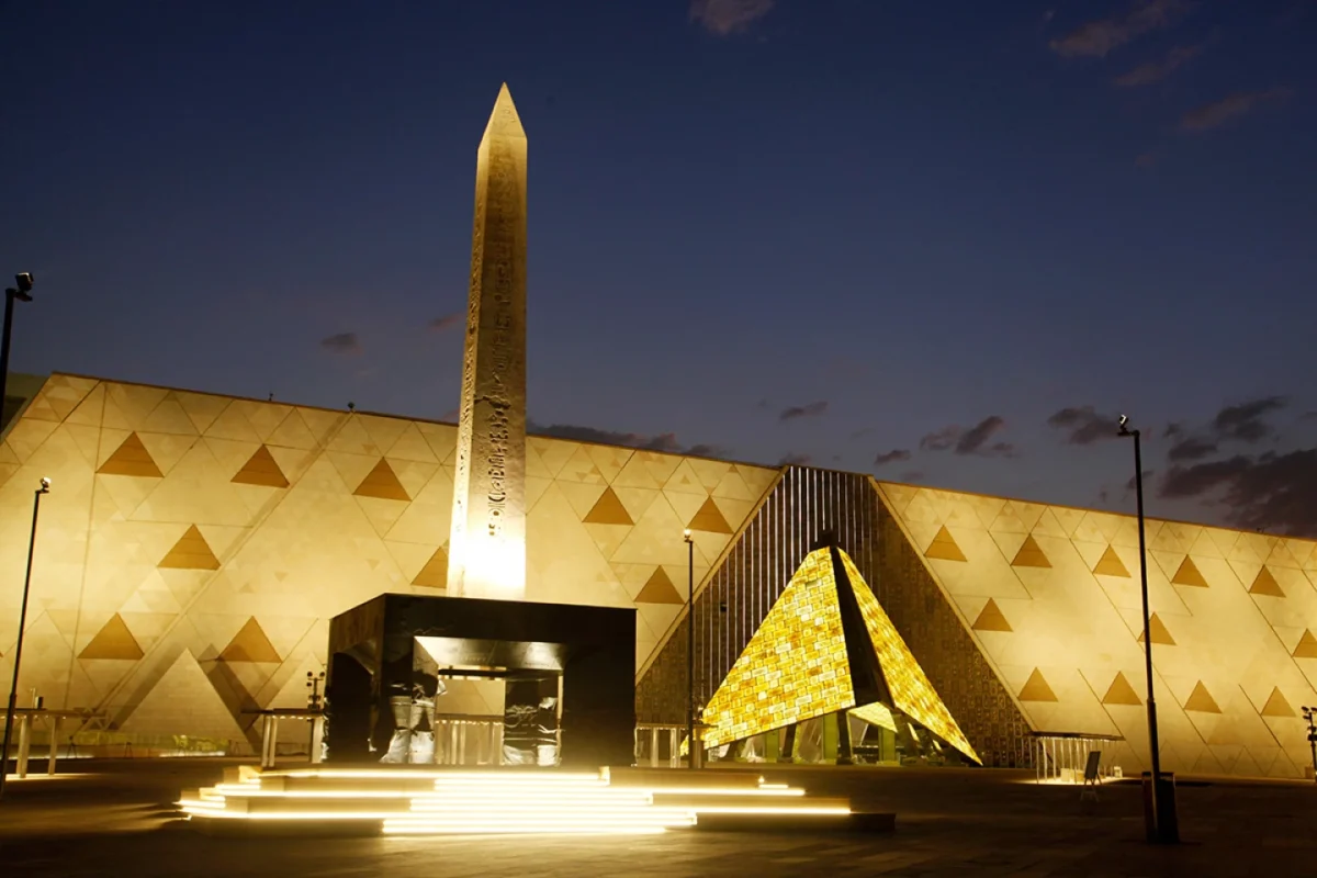 نمای شبانه موزه بزرگ مصر با ابلیسک روشن و هرم طلایی نورانی در ورودی