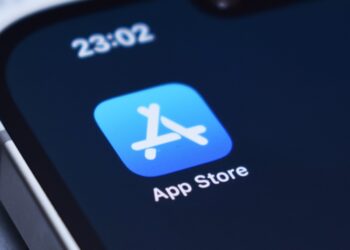 نمای نزدیک از آیکون اپ استور (App Store) بر روی صفحه نمایش یک گوشی هوشمند، با ساعت "23:02" در بالا.