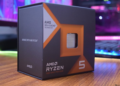 جعبه بسته‌بندی پردازنده AMD Ryzen 5 (7000 Series) با تکنولوژی 3D V-CACHE در یک نمای نزدیک روی یک میز، با پس‌زمینه سیستم کامپیوتری روشن.