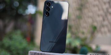 نمای پشت گوشی هوشمند مشکی رنگ سامسونگ (احتمالاً یک مدل Galaxy A یا S جدید) که ماژول دوربین سهگانه با لنزهای جداگانه را نشان میدهد و روی یک سطح سنگی در فضای باز قرار گرفته است.