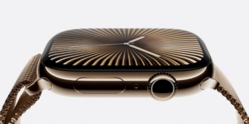 نمای نزدیک از یک اپل واچ با قاب طلایی و بند مشبک فلزی طلایی، که یک واچفیس با الگوی پرتوهای طلایی و سیاه را نمایش میدهد.