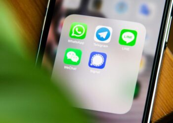 صفحه‌ی اصلی گوشی آیفون با آیکون‌های چندین برنامه پیام‌رسان (WhatsApp، Telegram، LINE، WeChat و Signal) که توسط یک گیاه سبز در پیش‌زمینه قاب شده‌اند.