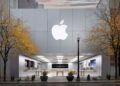 نمای بیرونی یک فروشگاه خرده‌فروشی اپل (Apple Store) با لوگوی بزرگ اپل روی نمای فلزی و درختان زرد پاییزی در جلوی آن.