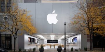 نمای بیرونی یک فروشگاه خرده‌فروشی اپل (Apple Store) با لوگوی بزرگ اپل روی نمای فلزی و درختان زرد پاییزی در جلوی آن.