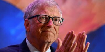 بیل گیتس با عینک و کت و شلوار در حال کف زدن در یک رویداد.