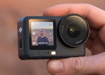 یک دوربین اکشن DJI Osmo Action 6 در دست، که صفحه نمایش جلویی آن یک سلفی از کاربر در محیط بیرون را نمایش می‌دهد.